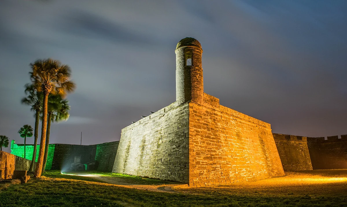 Castillo de San Marcos lit at night beside palm trees, on the evening route of St. Augustine carriage tours